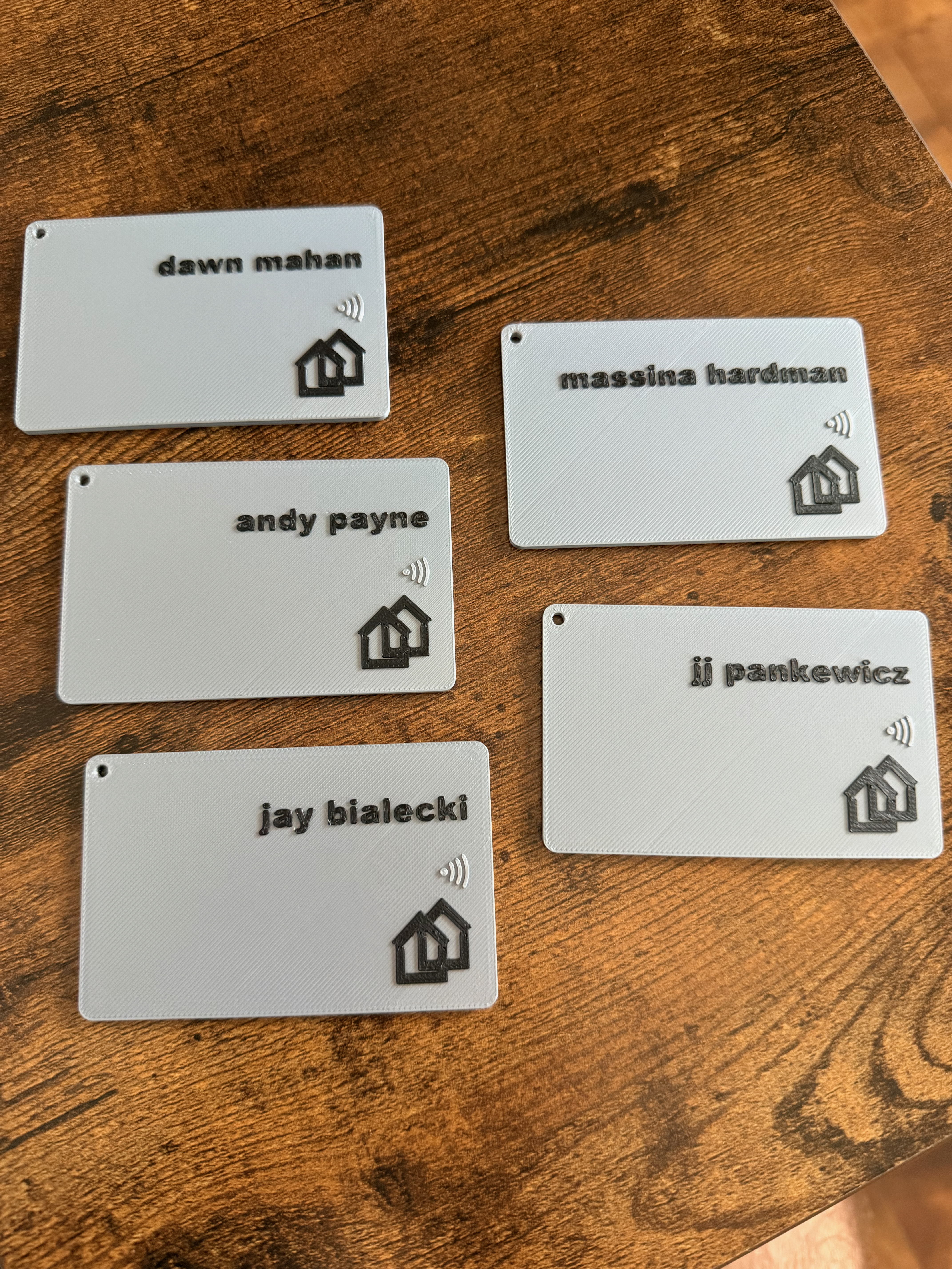 Five white business-card style NFC tags laid out on a wood surface, each personalized